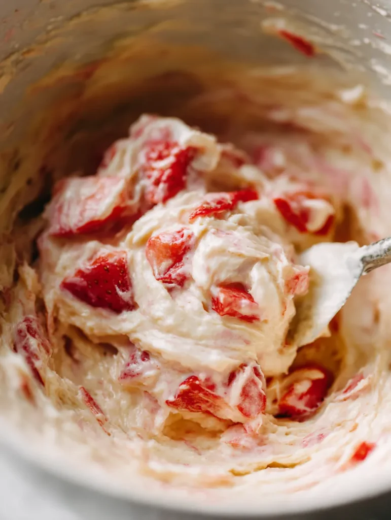 Folding fresh strawberry pieces into cake batter for even fruit distribution